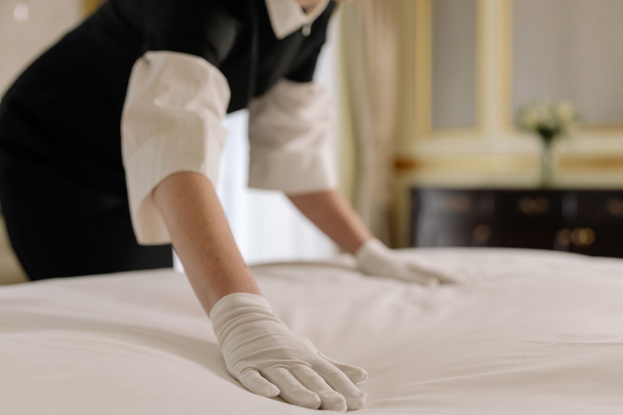 Services-03 A housekeeper straightening the bed linens in a well-appointed hotel room.