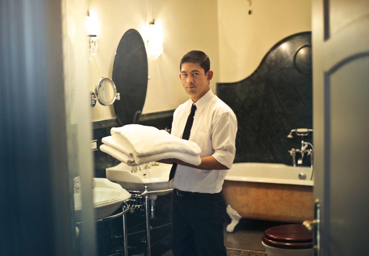 Services-01 A hotel employee holding towels in a luxury bathroom with elegant decor.