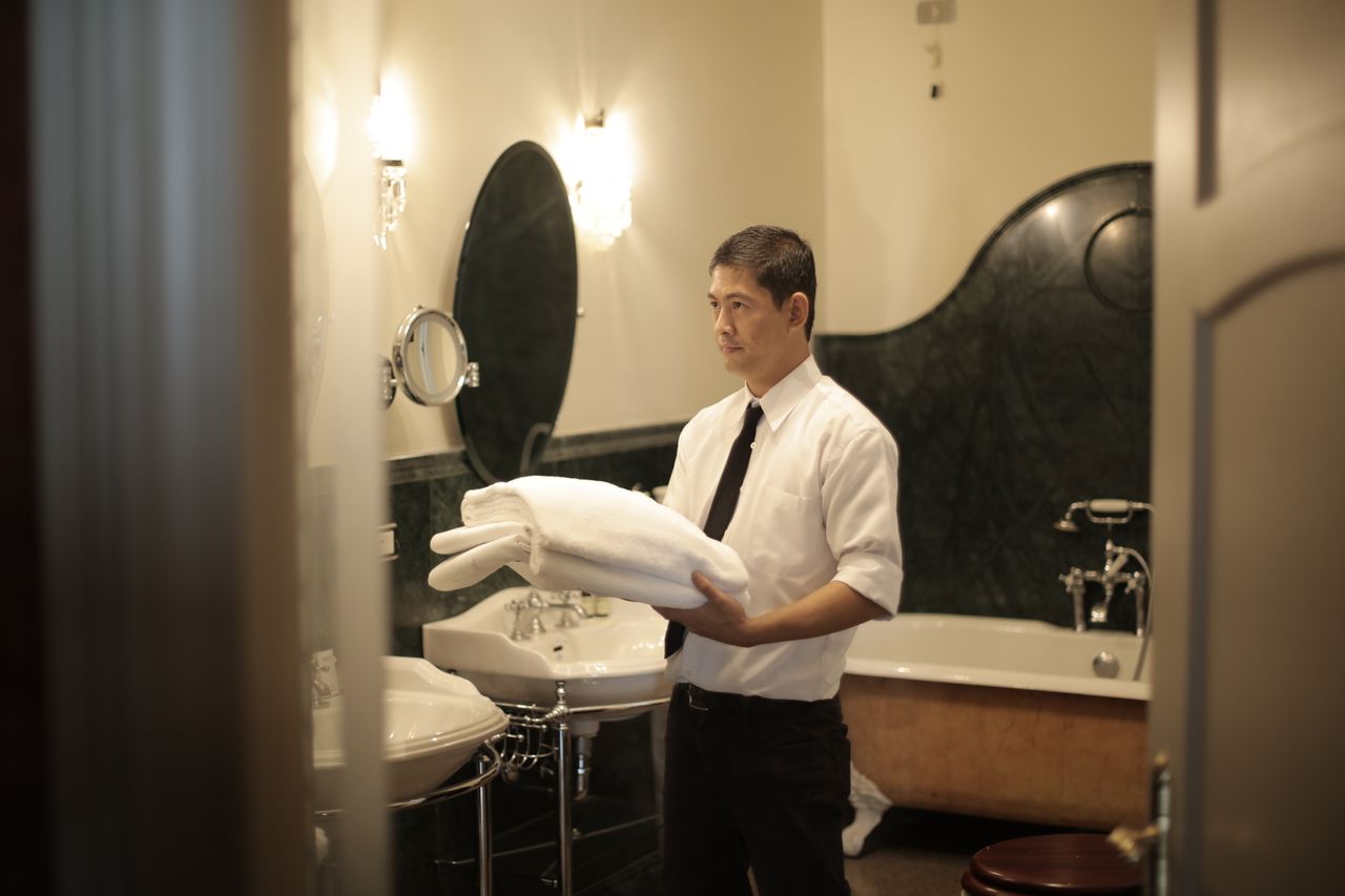 creative Side view of young male employee holding stack of white towels while standing in bathroom of luxury hotel