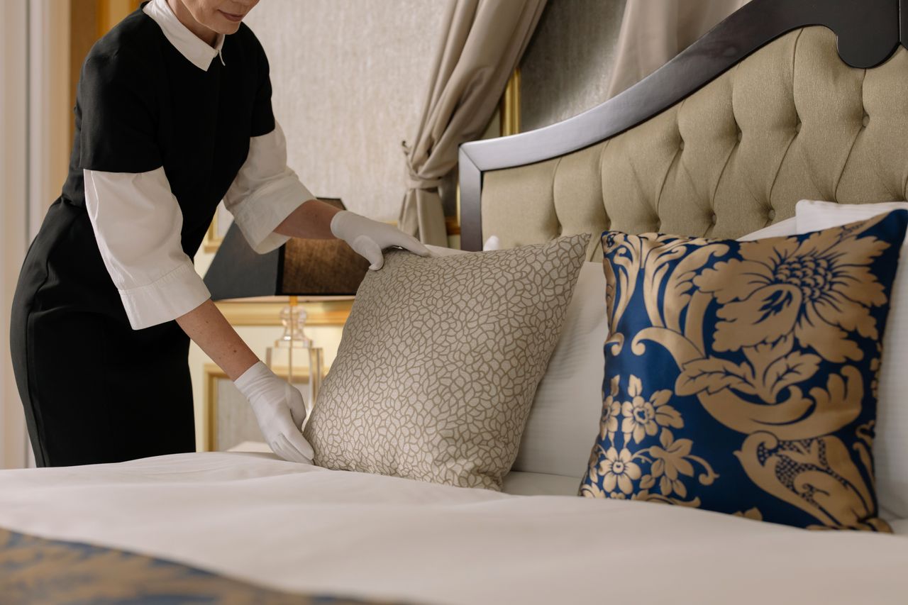 why-choose-us A chambermaid arranges pillows in a luxurious hotel room, showcasing comfort and elegance.